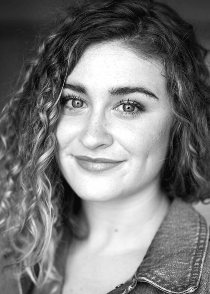 Brooke Sweeney headshot, smiling with curly hair and denim jacket.