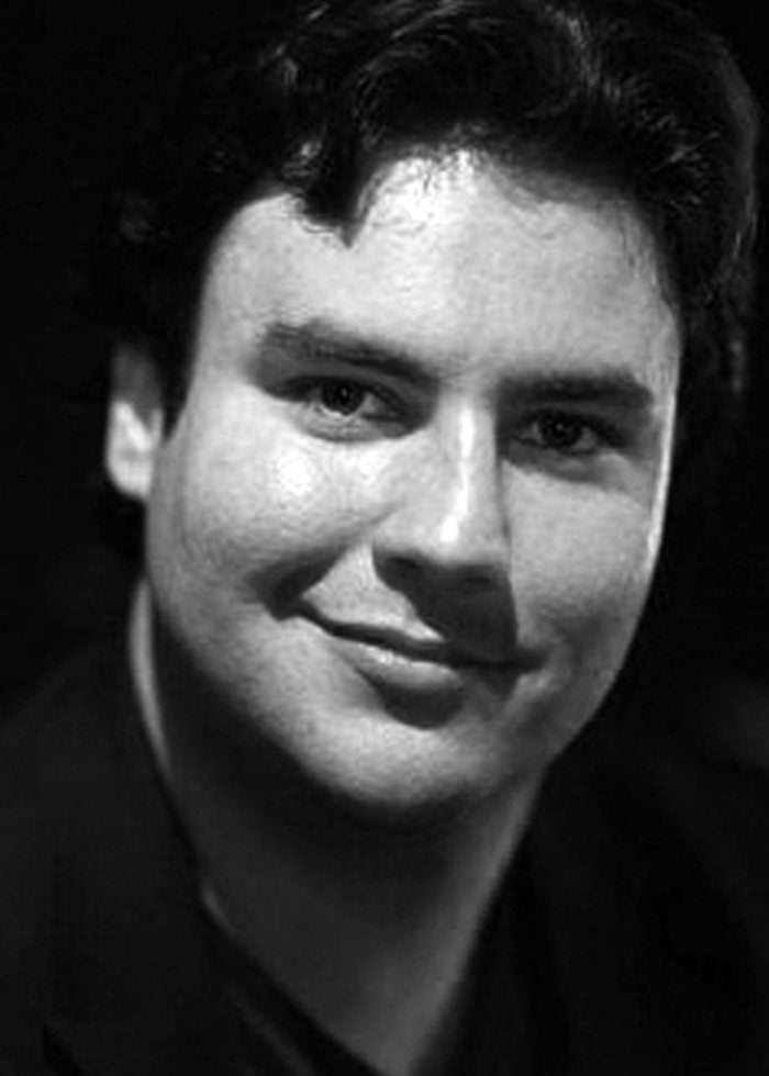 Caleb Hoyer smiling, looking at the camera in a black and white portrait.