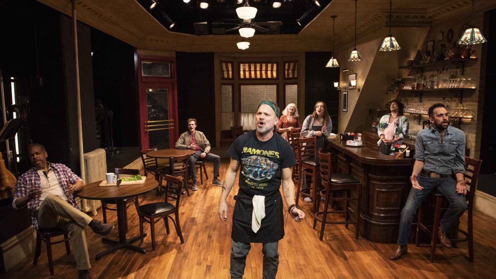 Cast of Cornelia Street in a diner setting. A man in a Ramones t-shirt is center stage.