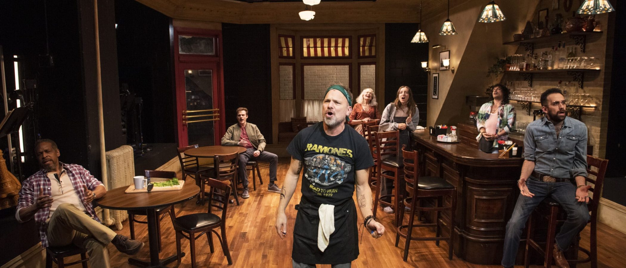 Cast of Cornelia Street in a diner setting. A man in a Ramones t-shirt is center stage.