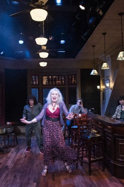 A lively scene in a Cornelia Street bar, featuring a woman singing and patrons seated at tables and the bar.