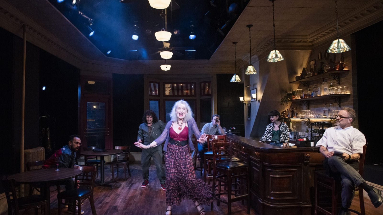 A lively scene in a Cornelia Street bar, featuring a woman singing and patrons seated at tables and the bar.