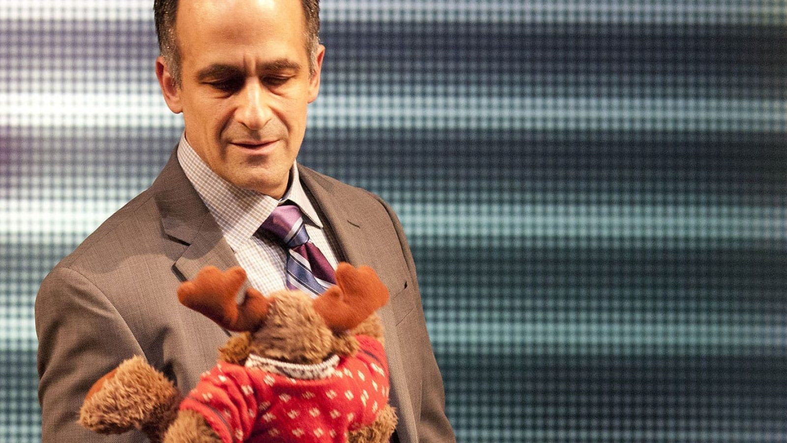 Man in suit holding a moose plush toy