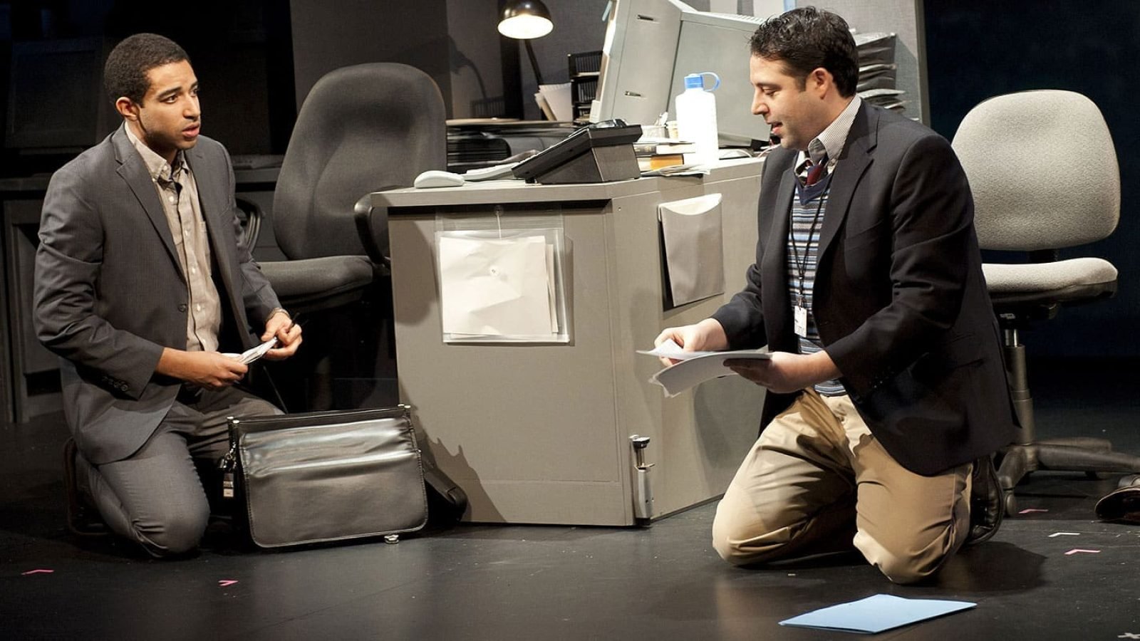 Two men in suits kneel, reviewing documents in an office setting. CQ/CX