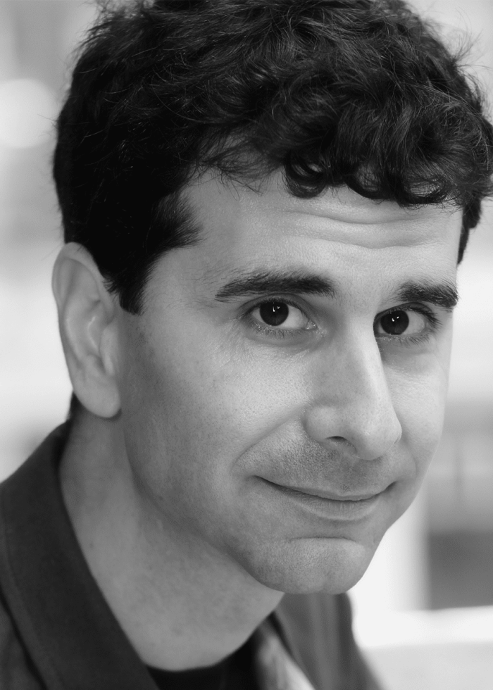 John Cariani, author and actor, smiling in a black and white portrait.