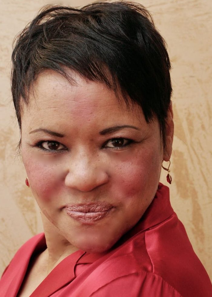 Close-up portrait of Caroline Clay wearing a red top and earrings, looking directly at the camera.