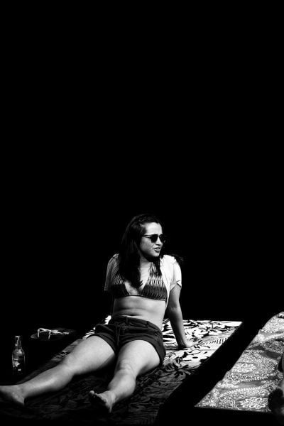 Two women relax on beach towels, wearing sunglasses and bikinis.