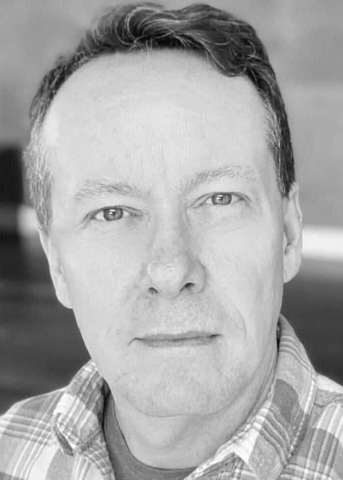 Christopher Liam Moore, headshot portrait in plaid shirt.