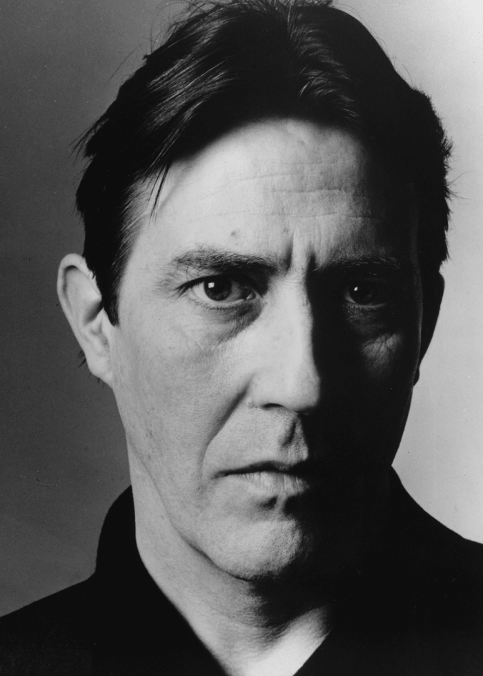 Ciarán Hinds in a black and white portrait, looking directly at the viewer.