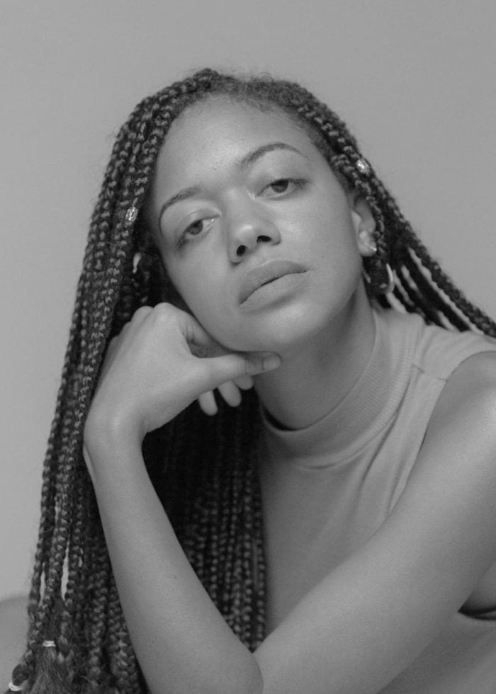 Cindy De La Cruz portrait in black and white, resting chin on hand, with braided hair.