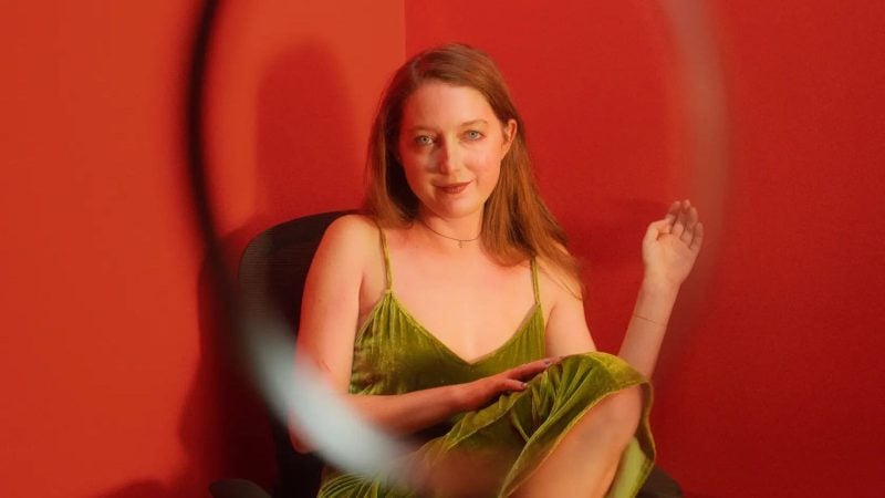 Clare Barron in a green velvet dress, seated in a red-walled room.
