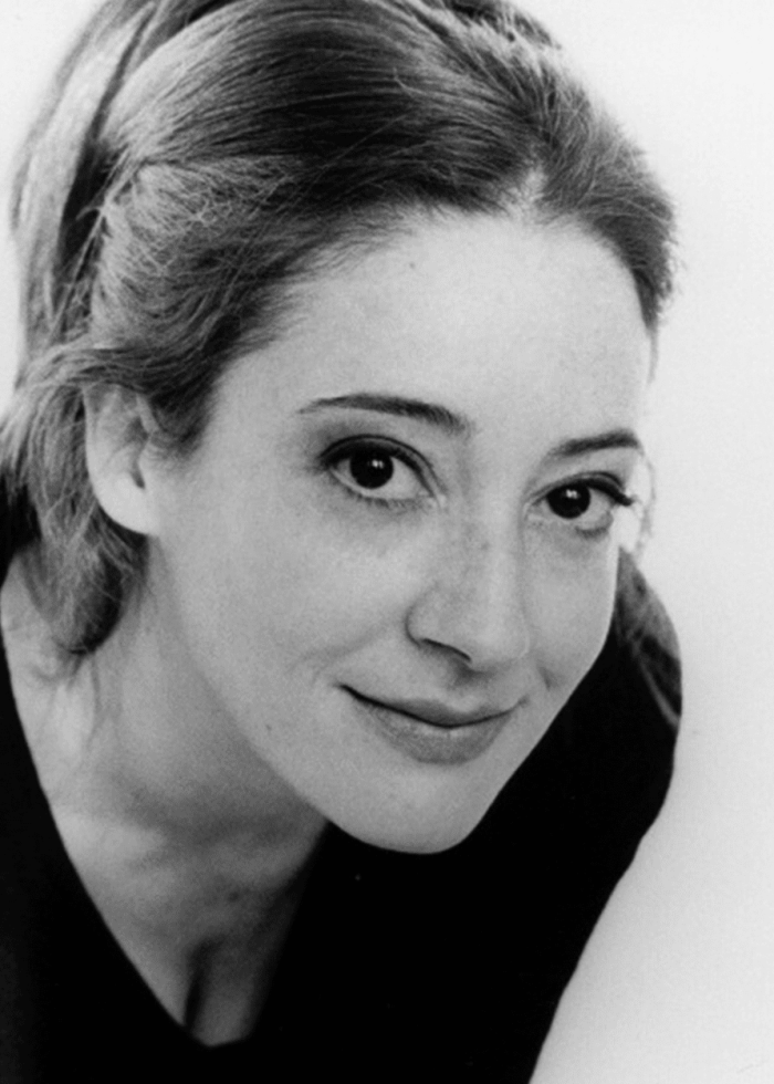 Clea Lewis smiling, looking up at the camera in a black and white portrait.