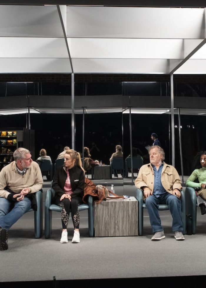 People waiting in a modern medical office, possibly related to "I'm Revolting." A doctor holds a clipboard.