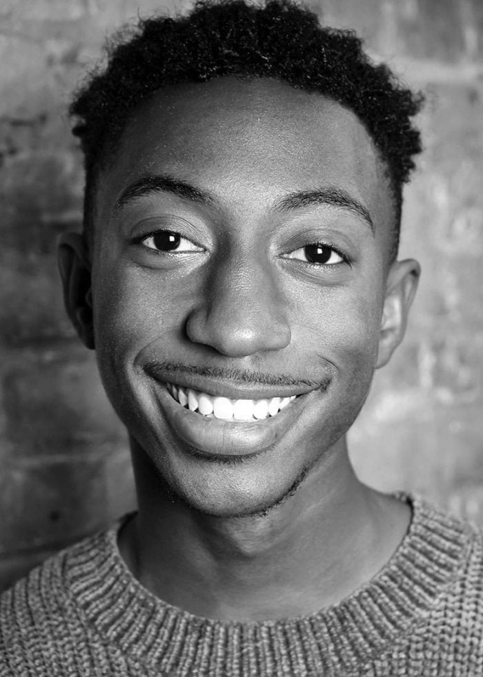 Danté Crichlow smiling, wearing a sweater, in a black and white portrait.