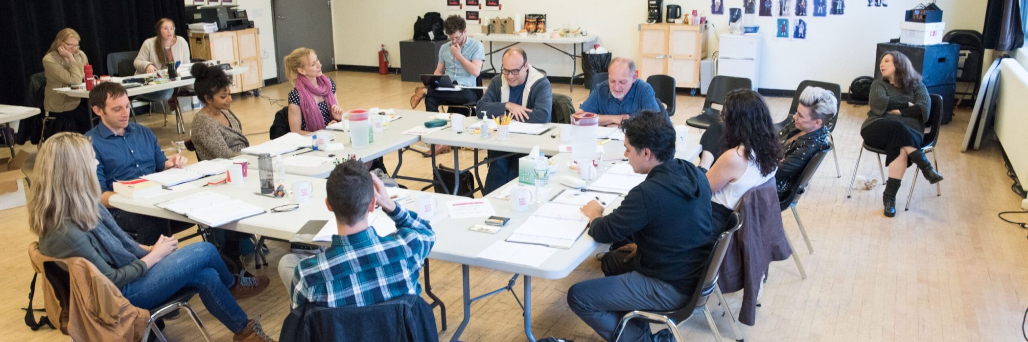 Group of people in a rehearsal setting, discussing a script during playwriting development.