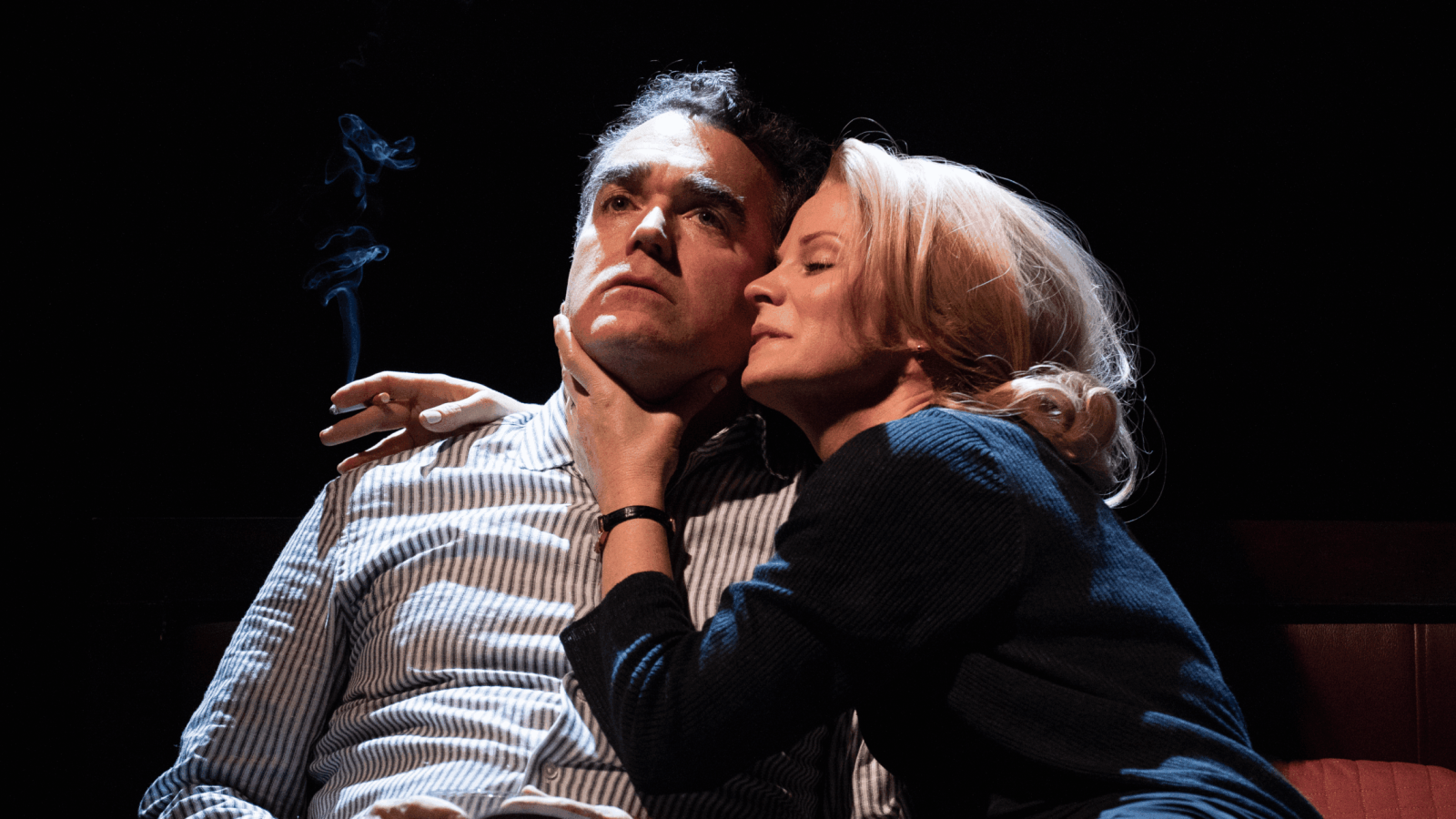 A man and woman embrace intimately, the man smoking a cigarette.