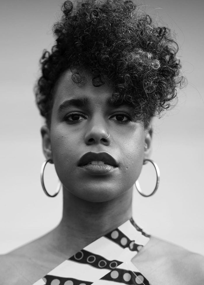 Black and white portrait of Danaya Esperanza with curly hair and hoop earrings.