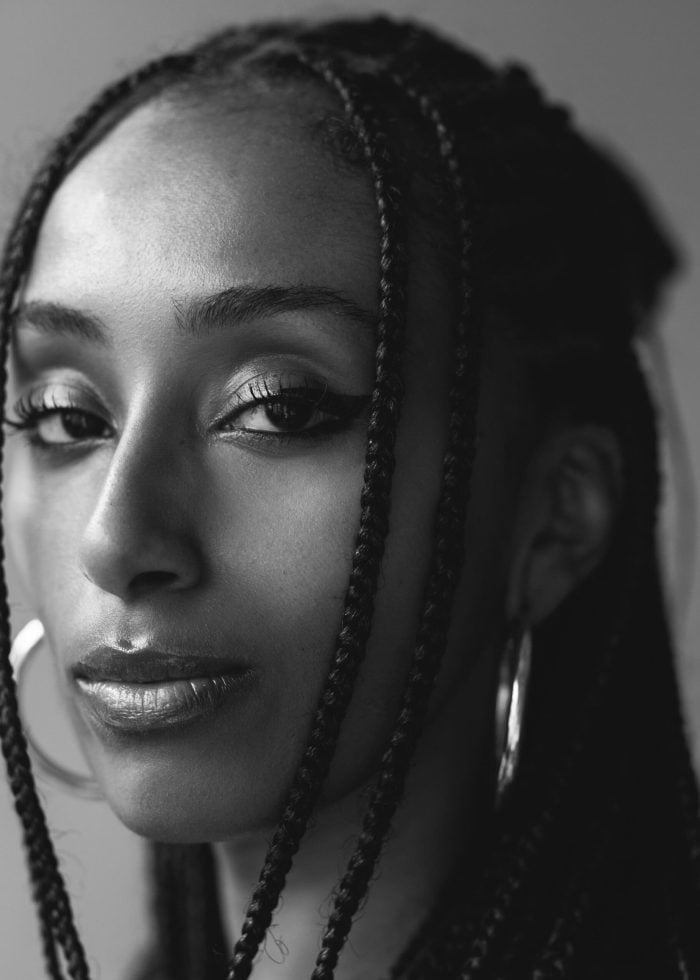 Portrait of a woman with braided hair and hoop earrings, looking at the camera