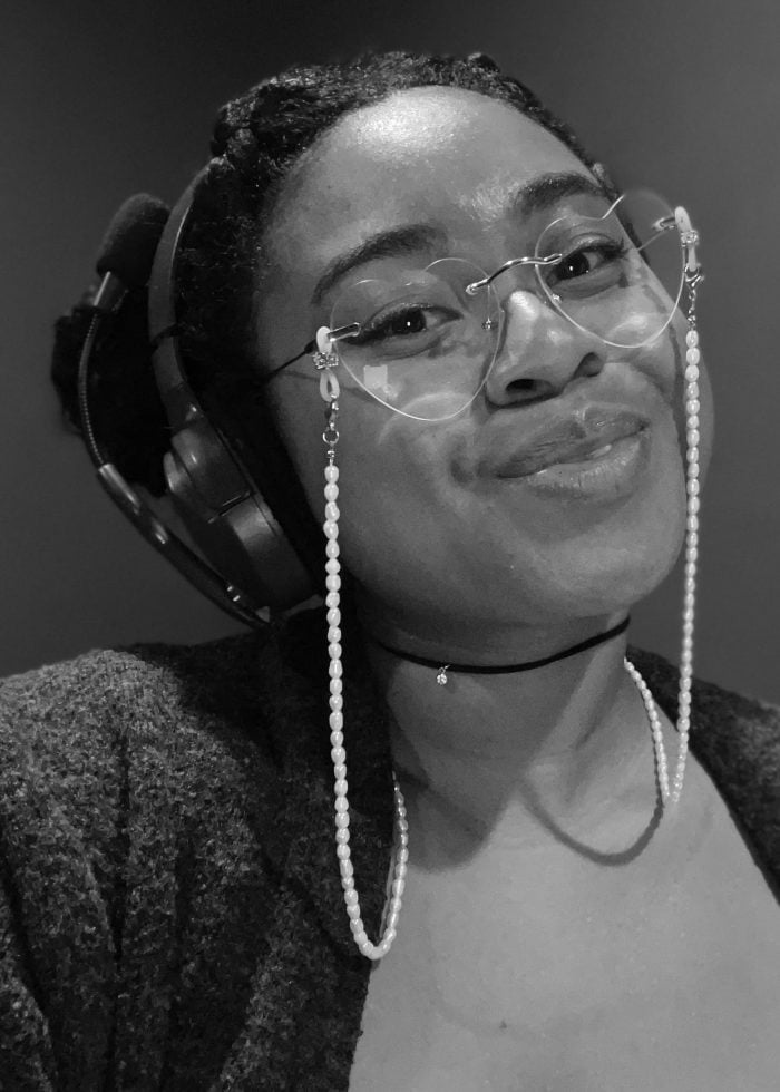 Woman with glasses and headset smiles. Pearl eyeglass chain.