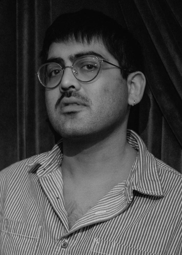 Man with mustache and glasses in striped shirt, Banna Desta