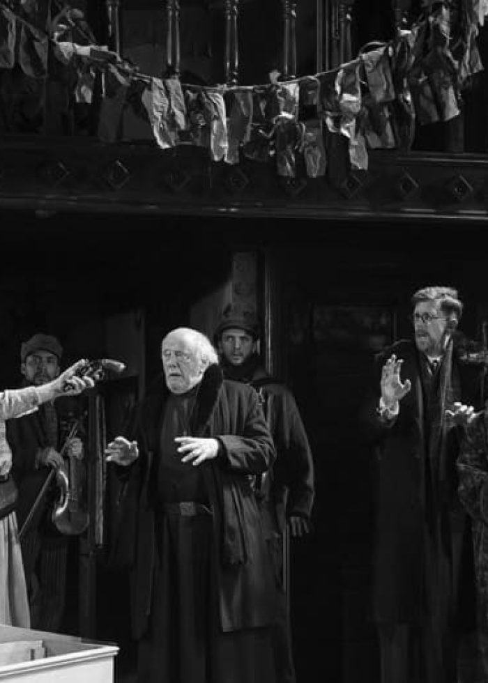 Scene from "Dying for It" play: actors in period costumes on stage, dramatic lighting.