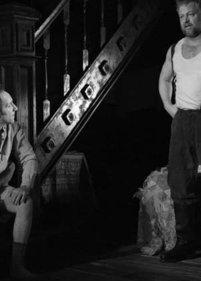 Two men in a dimly lit room during a performance of "Dying for It" at the Atlantic Theater Company.