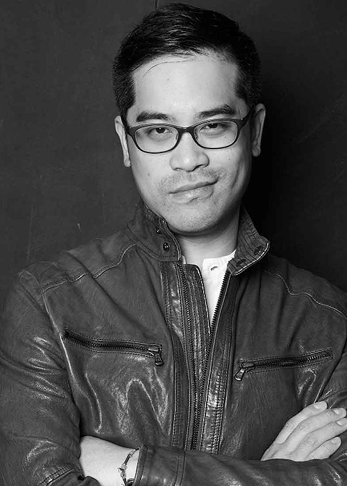 Ed Sylvanus Iskandar wearing glasses and leather jacket, looking at the camera.