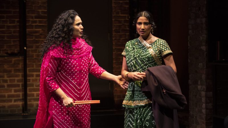 Two actresses in colorful traditional clothing perform on stage at the Atlantic Theater Company.