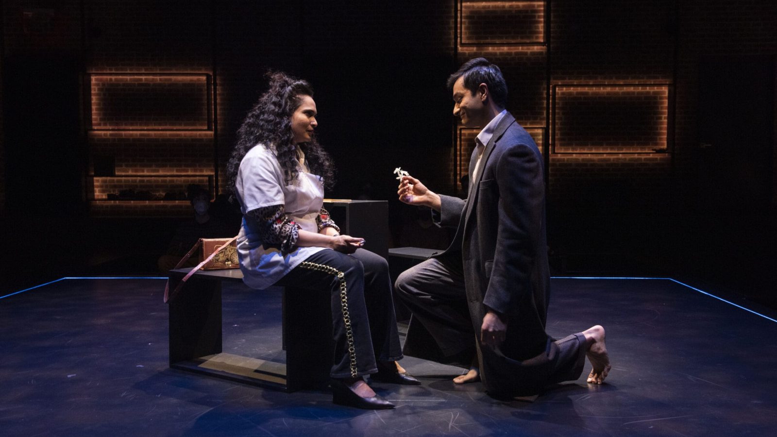 A man kneels and offers flowers to a woman in a theatrical production of Elyria.