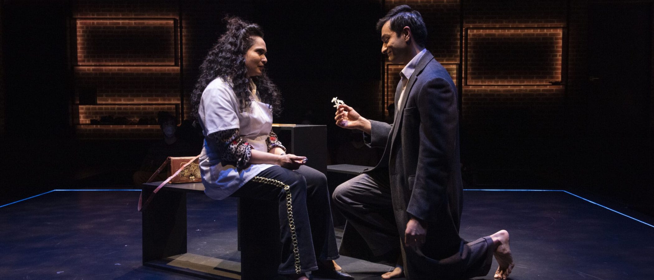 A man kneels and offers flowers to a woman in a theatrical production of Elyria.