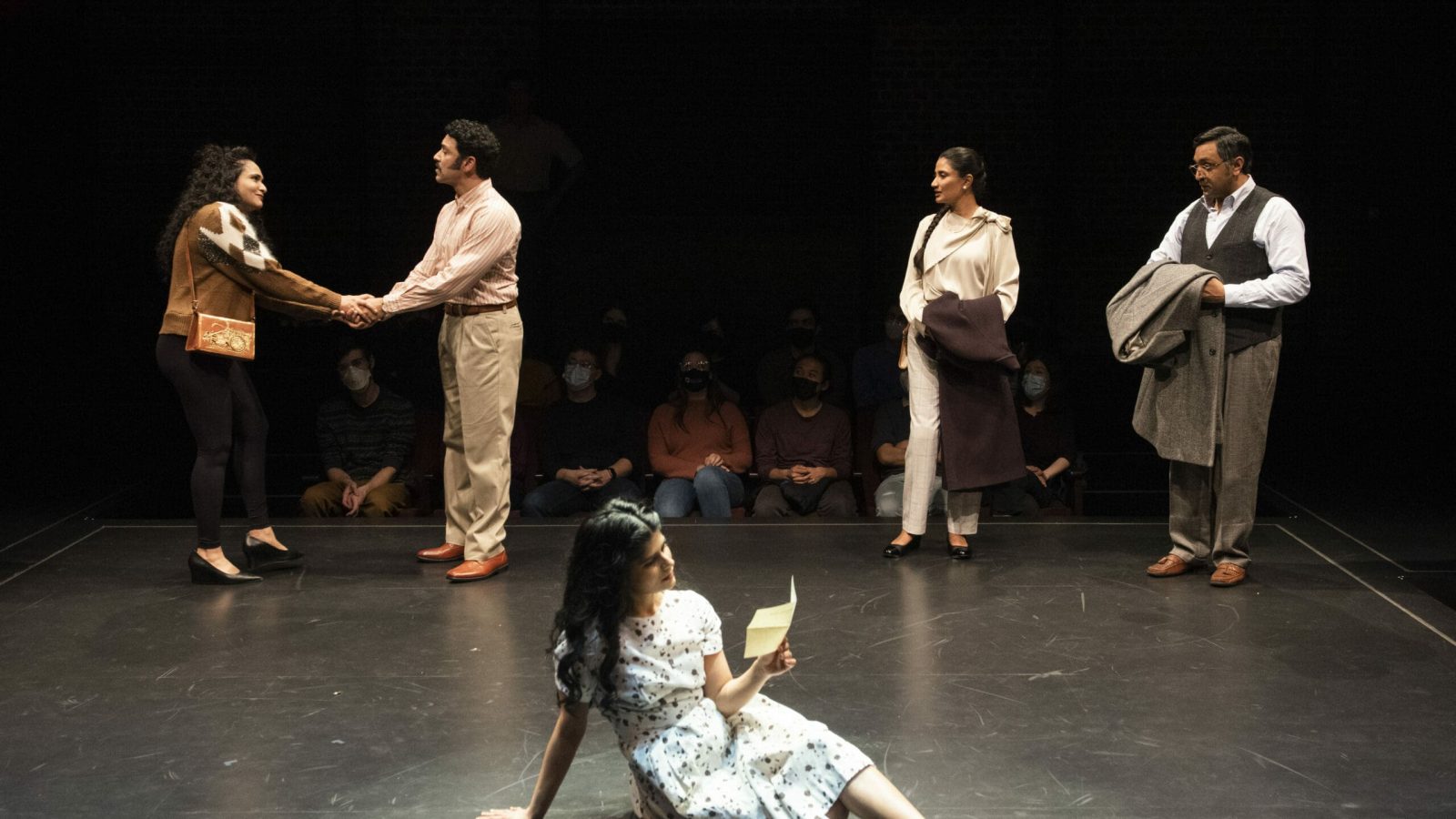 Four actors in a dramatic scene on stage, one woman sits reading a letter.
