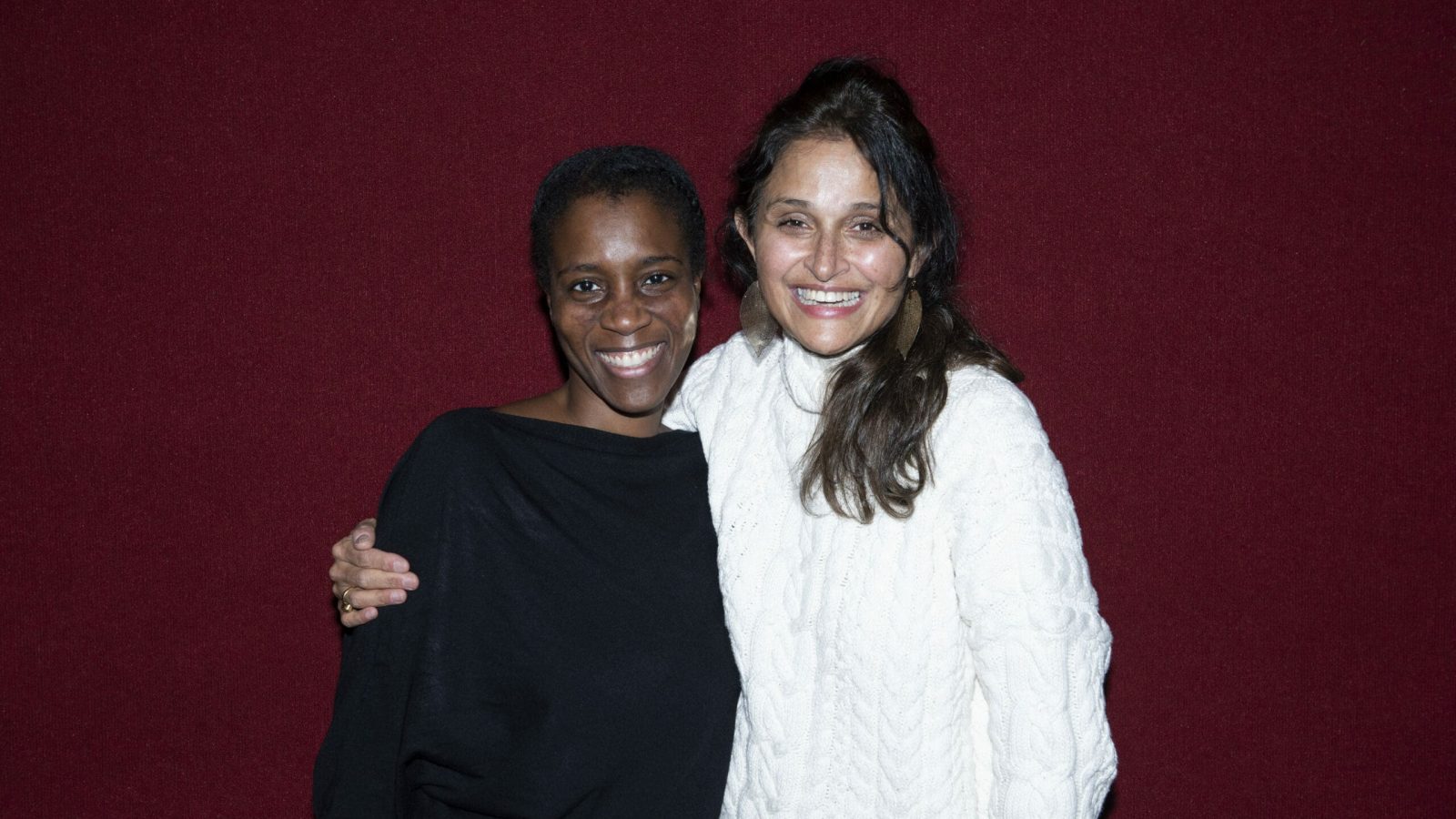 Two women smiling together, one wearing a black sweater and the other a white sweater.