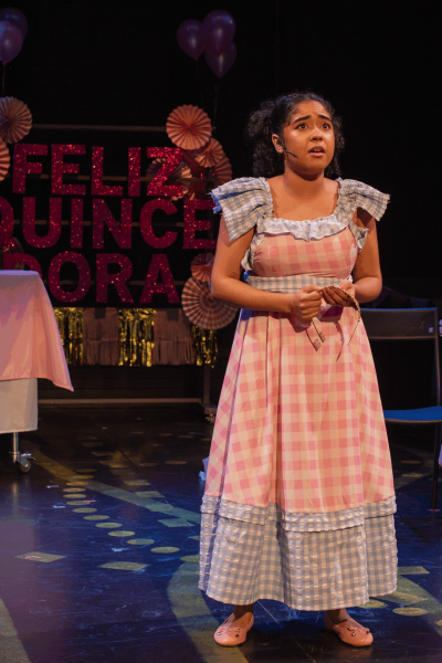 Young actress in a pink gingham dress performs in El Otro Oz, with a "Feliz Quince Años" backdrop.