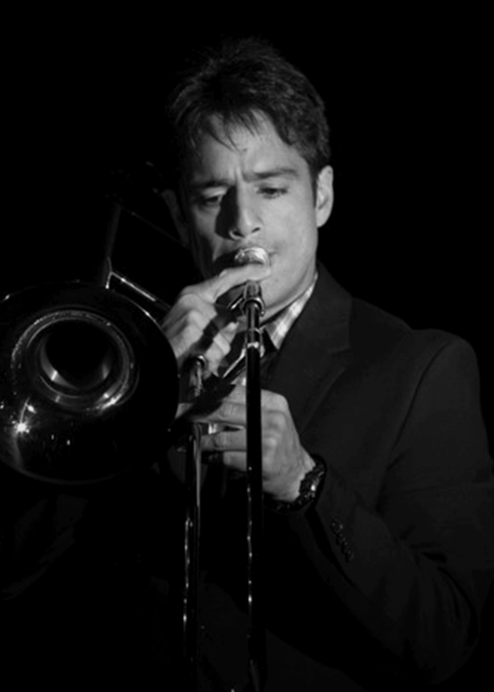 Eddie Venegas playing trombone in a spotlight, wearing a suit and focused on his music.