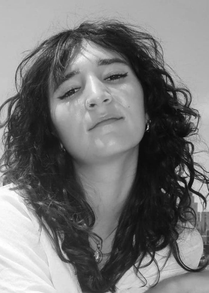 Eliana Theologides Rodriguez looking at the camera with curly hair and a cityscape background.