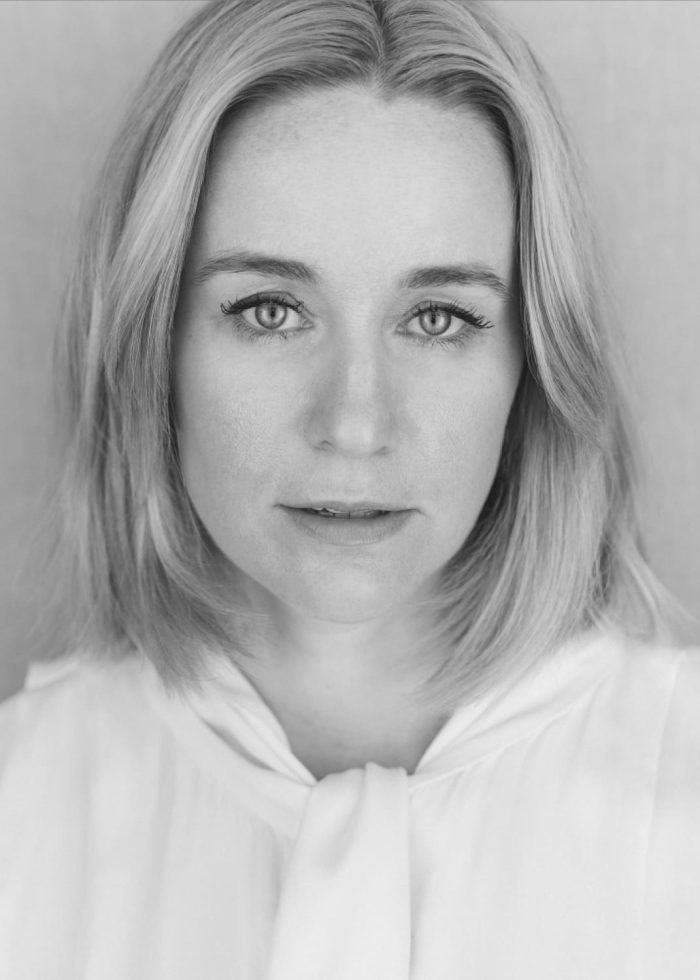 Emily Cass McDonnell headshot, looking directly at the camera in a white blouse.
