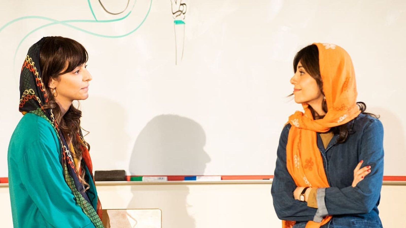 Two women in headscarves converse in front of a whiteboard.
