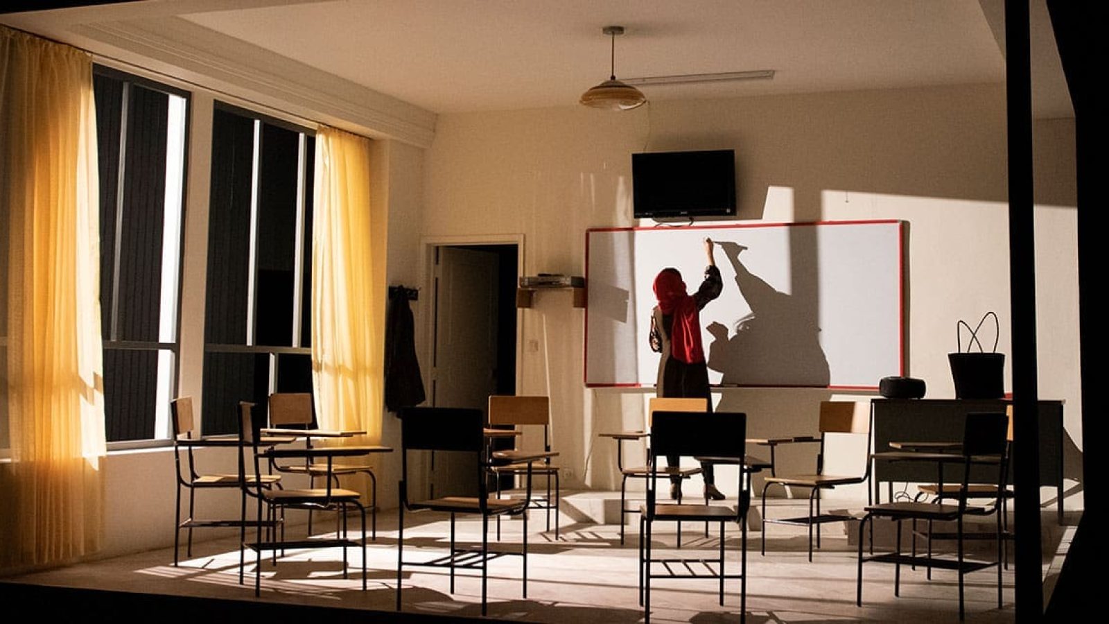 Woman in hijab writing on whiteboard in classroom
