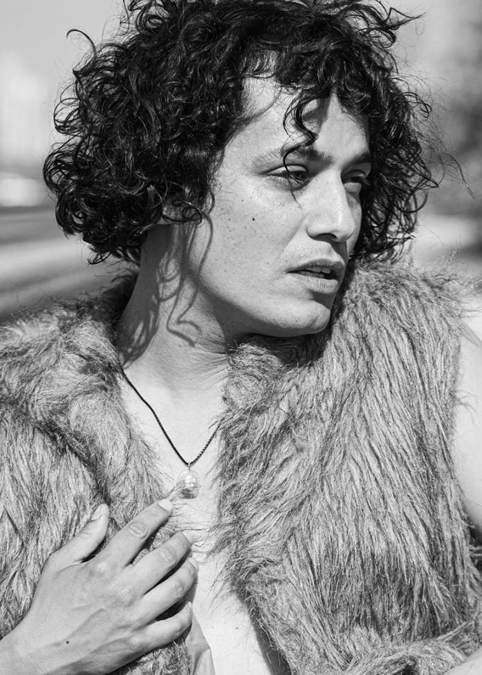 Esteban Andres Cruz in a faux fur vest, looking thoughtful with curly hair.