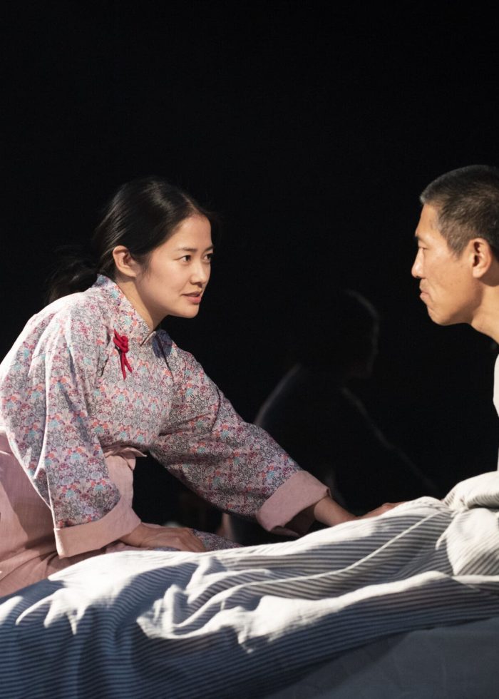 Actors in a scene from "The Far Country" by Lloyd Suh, a Pulitzer Prize finalist. A woman leans towards a man on a bed.