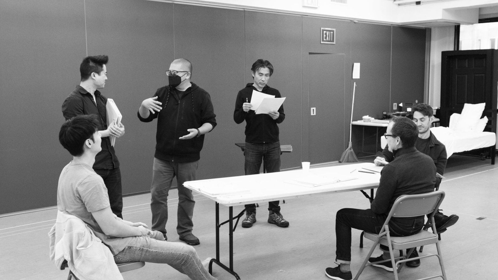 Actors and director in rehearsal for "The Far Country," reviewing scripts at a table.