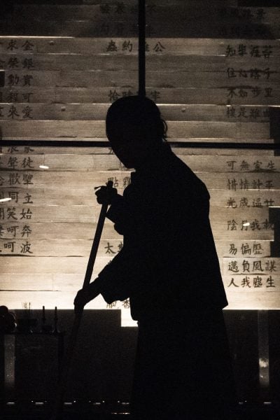 Silhouette of a person sweeping in a dimly lit room with Chinese characters on the wall.
