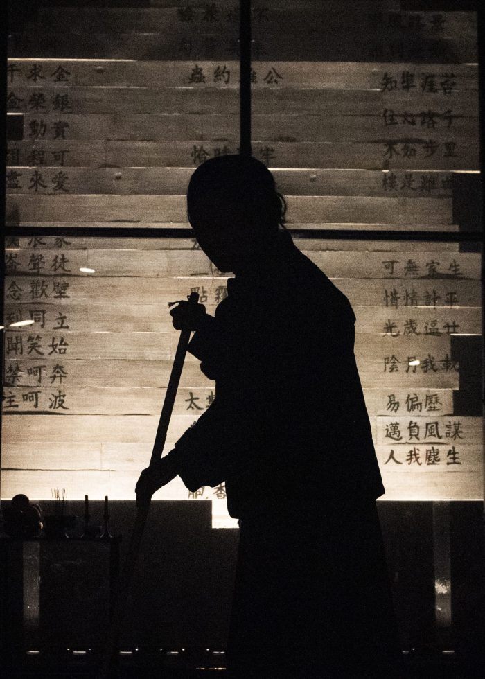 Silhouette of a person sweeping in a dimly lit room with Chinese characters on the wall.