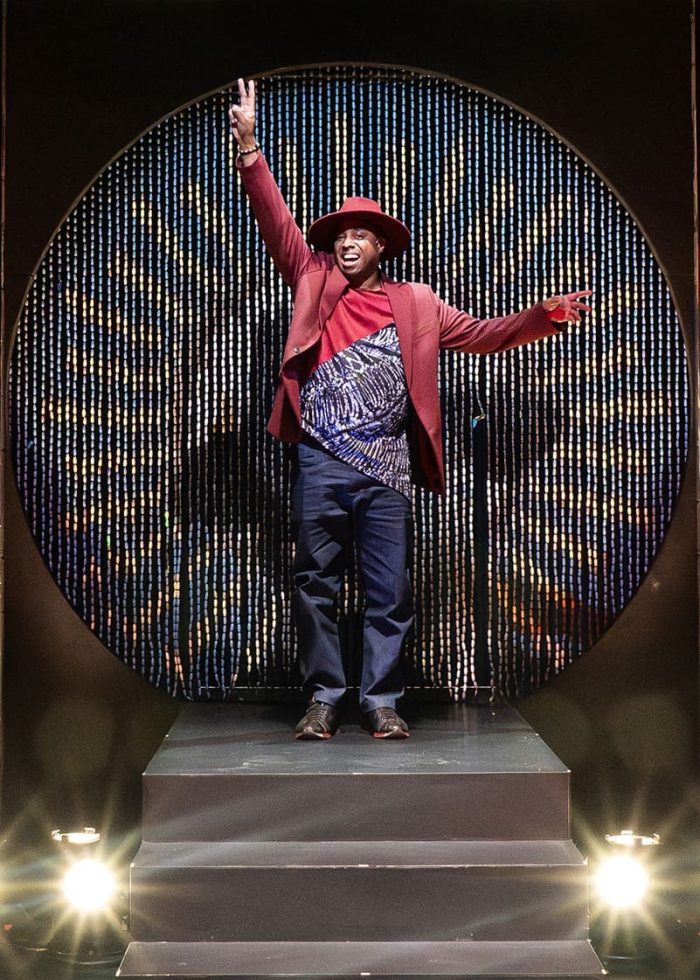 Man in red blazer and hat on stage, celebrating with peace sign, Freeky introduction