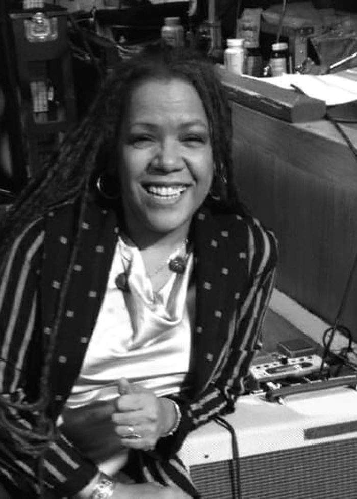 Felicia Collins smiling, wearing a striped jacket and sitting near audio equipment.