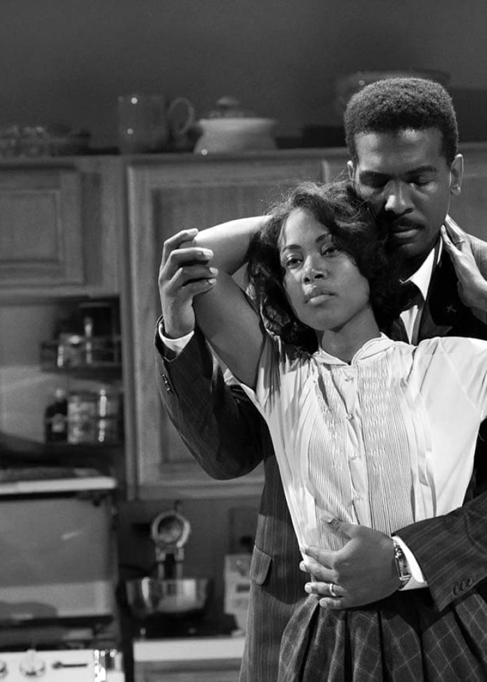 Couple embracing in a vintage kitchen setting, a scene from a play.