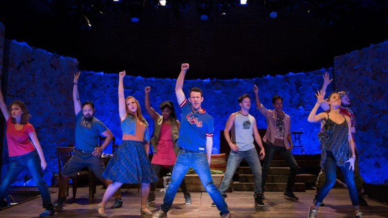 Performers on staged with one hand raised against a blue background