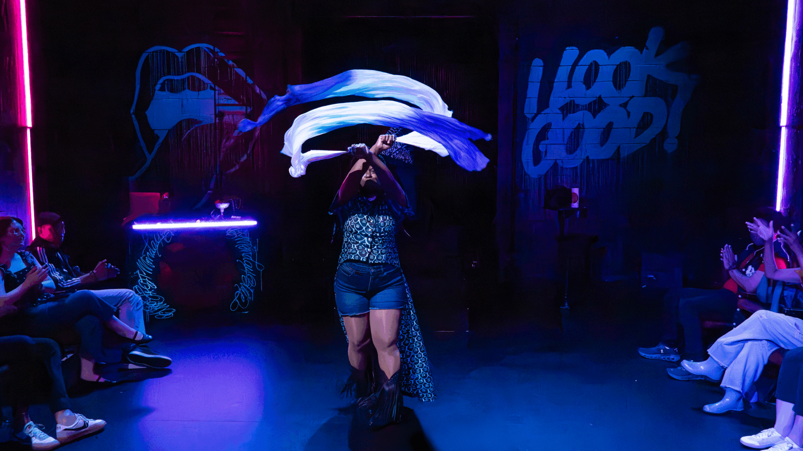 Fashion show performer with scarf in front of graffiti art that says "I LOOK GOOD!