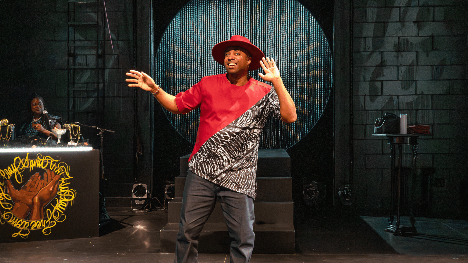 Man in red shirt and hat on stage, gesturing. DJ booth visible. A Freeky Introduction.