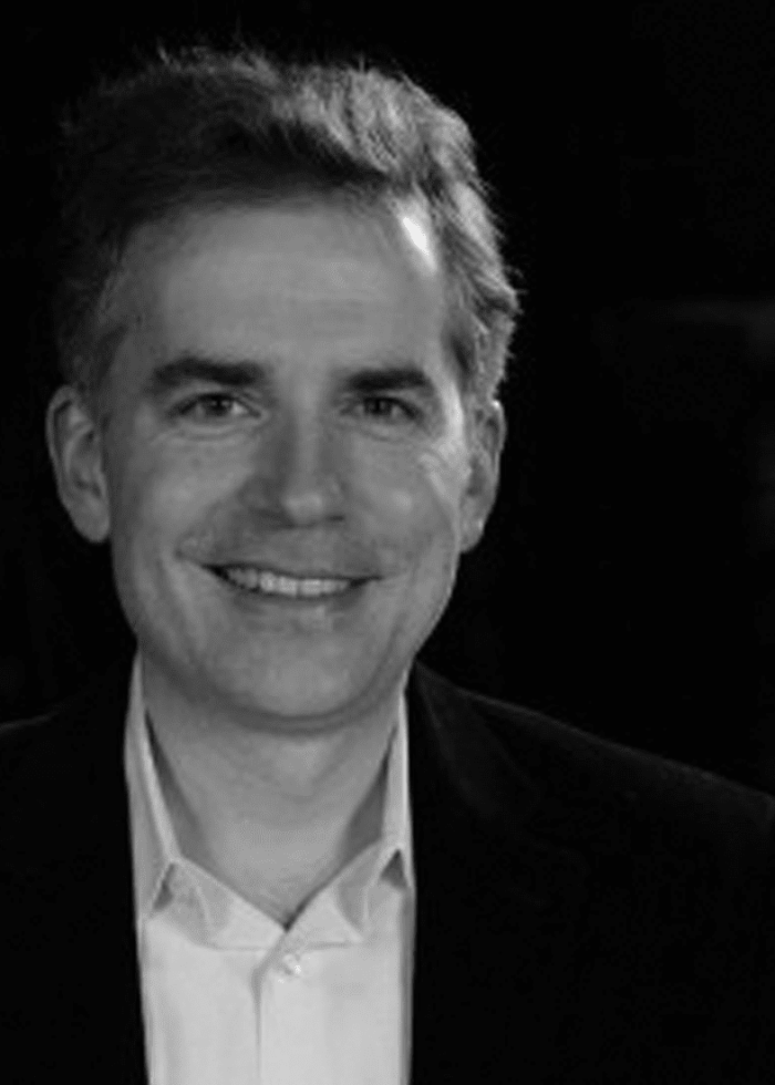 George Brant smiling, wearing a dark blazer and white shirt